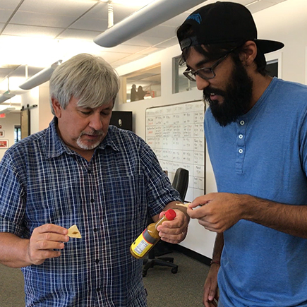 Pat inspects the bottle of hot sauce as Shaq waits for his share.